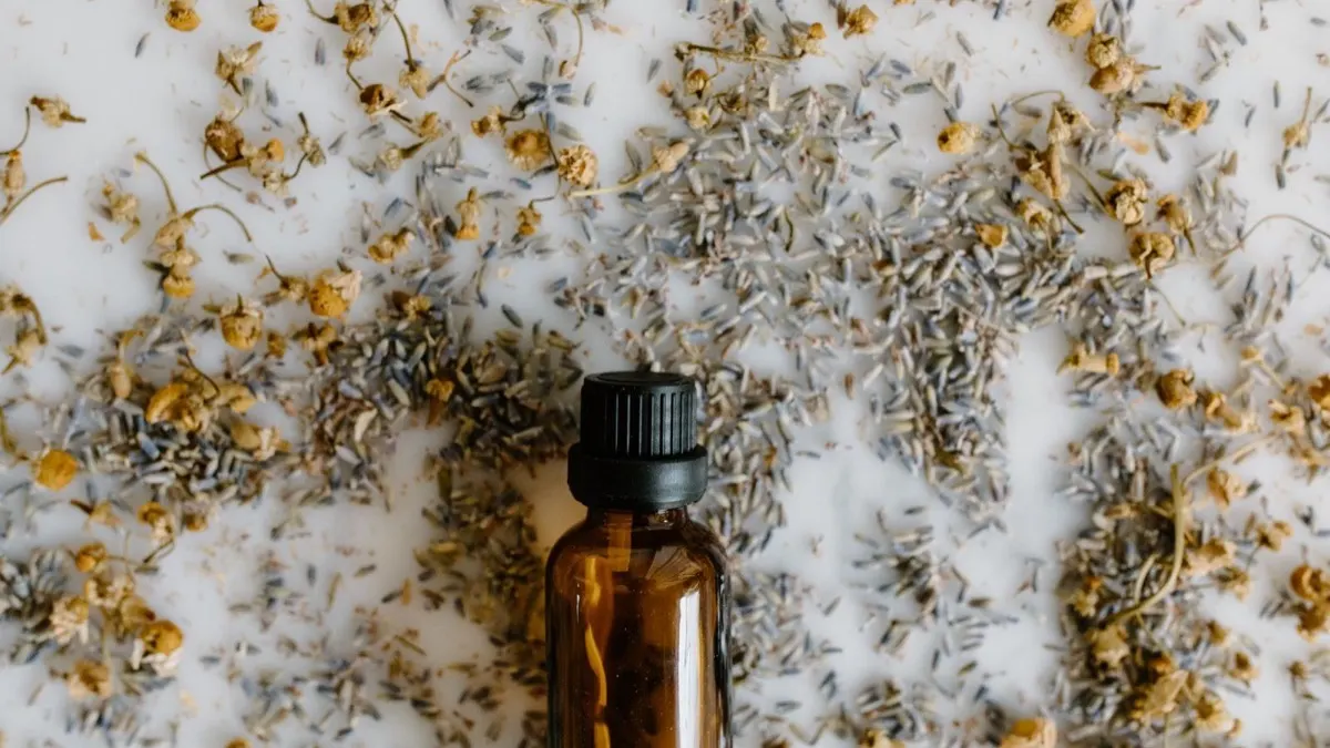 Brown glass dropper bottle surrounded by scattered dried lavender and chamomile flowers on a white surface